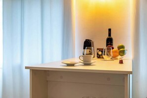 Ein kleiner Tisch mit einer Kaffeemaschine, einer Flasche, einer Tasse und einer Obstschale.