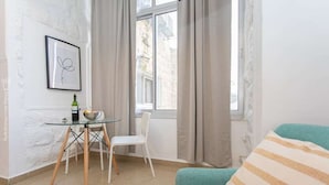 Ein Zimmer mit einem Glastisch, einem weißen Stuhl, einem salbeengrünen Sofa und einem gerahmten Bild an der Wand.