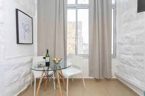 A room with a glass table, white chairs, a bottle, and a bowl of fruit.
