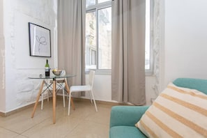 A room with a dining table, chairs, a sofa, and a window with curtains.