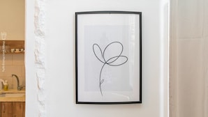 Ein gerahmtes Kunstwerk mit einer einfachen Linienzeichnung einer Blume an einer weißen Wand.