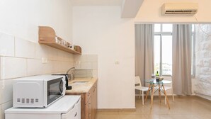Eine kompakte Küche mit Mikrowelle, Spüle und Holzschränken. Es gibt einen Essbereich mit Tisch und Stühlen, sowie ein Fenster mit Vorhängen.