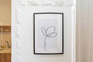 A framed artwork with a simple line drawing of a flower on a white wall.
