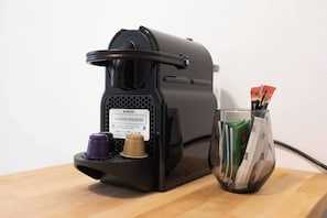 A Nespresso coffee machine with a coffee pod holder and a glass of coffee pods on a wooden surface. - Downtown Haifa Studio 217, Port View, AC, WiFi (Haifa)