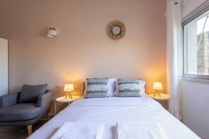A hotel room with a bed, two bedside lamps, a chair, and a wall-mounted light fixture. - Port city haifa - Studio 218 (Haifa)