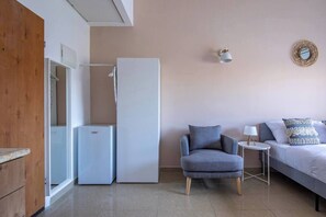 A bedroom with a bed, a chair, a small table, a lamp, and a refrigerator. - Port city haifa - Studio 218 (Haifa)