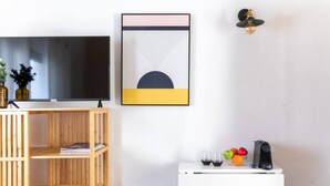 A modern living room with a flat-screen TV, a wooden shelving unit, a white cabinet with a coffee machine, and a framed abstract artwork. - Port city haifa - Studio 219 (Haifa)
