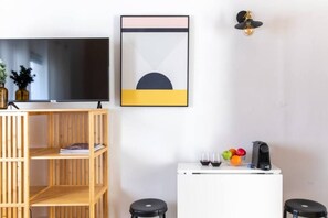 Ein modernes Wohnzimmer mit einem Flachbildfernseher, einer Holzhockeranlage, einem weißen Schrank mit Kaffeemaschine und einem gerahmten abstrakten Kunstwerk.