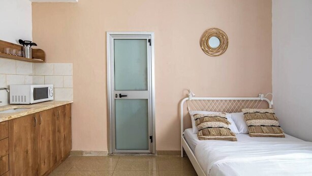 A bedroom with a bed, a bedside table, a microwave, and a door. - Port city haifa - Studio 219 (Haifa)