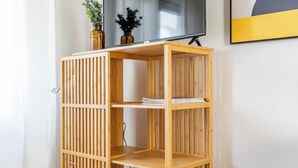 A wooden bookshelf with three shelves, a flat-screen TV mounted above it, and two decorative vases on the top shelf. - Port city haifa - Studio 219 (Haifa)