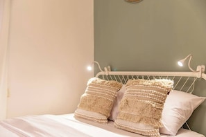 A bed with two textured pillows and a white headboard in a room with a green wall and a white ceiling.