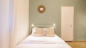 A bedroom with a bed, a door, and a wall-mounted circular mirror.