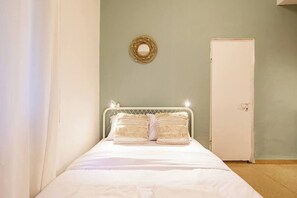 A bedroom with a bed, a door, and a wall-mounted circular mirror.