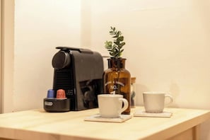 A coffee machine, a bottle with a plant, and two white cups on a wooden table.
