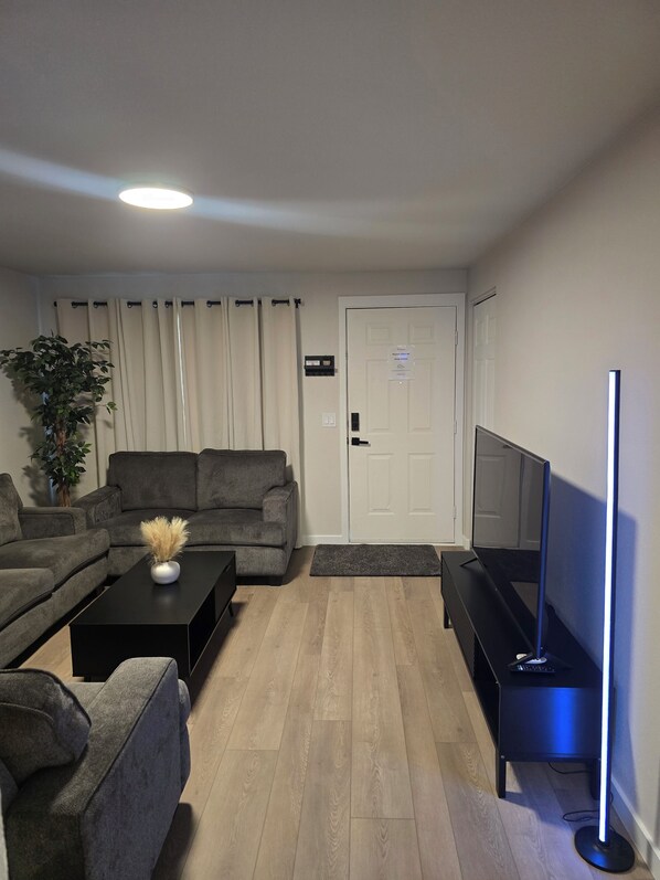 Ein Wohnzimmer mit einer Sofagarnitur, einem Couchtisch mit einer Vase, einem Flachbildfernseher und einer Stehlampe.