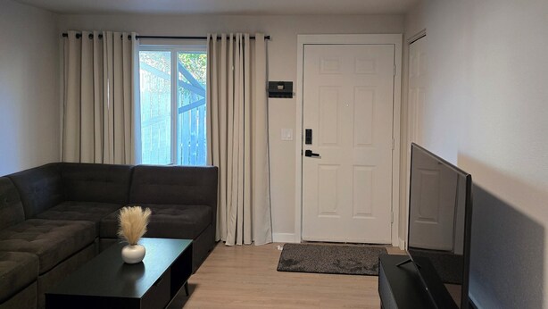 A modern living room with a sectional sofa, a coffee table with a vase, a flat-screen TV, and a door with a doormat.