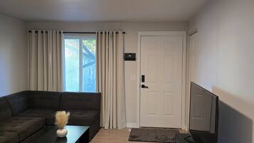 A modern living room with a sectional sofa, a coffee table with a vase, a flat-screen TV, and a door with a doormat.