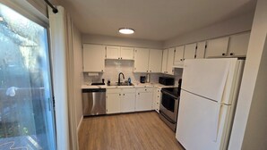 A modern kitchen with white cabinets, stainless steel appliances, and a wooden floor.