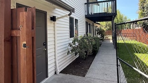 A two-story residential building with a covered front porch, a wooden gate, and a fenced backyard.