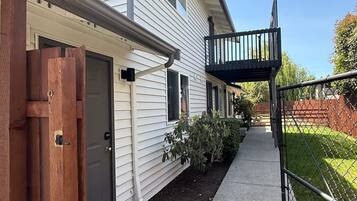 A two-story residential building with a covered front porch, a wooden gate, and a fenced backyard.