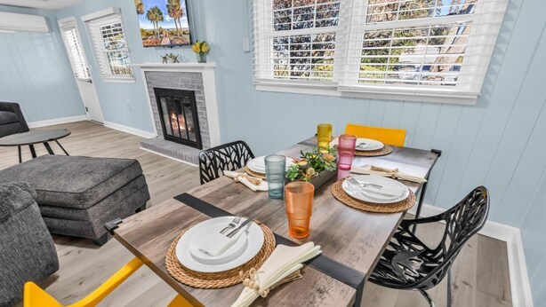 A dining area with a wooden table set for four, surrounded by modern chairs, a fireplace, and a view of the outdoors through large windows. - Sea Breeze 1019 near Ocean (North Myrtle Beach)