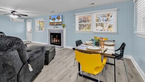 A living room with a fireplace, a dining area with yellow chairs, and a grey sofa. - Sea Breeze 1019 near Ocean (North Myrtle Beach)