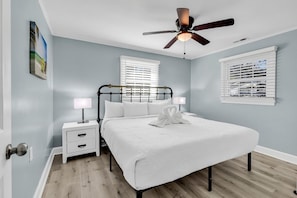 A bedroom with a bed, nightstands, a ceiling fan, and a window with blinds.
