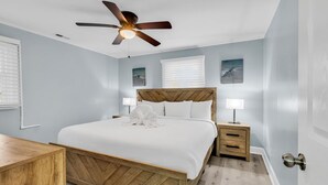 A bedroom with a wooden bed, a nightstand, a ceiling fan, and artwork on the walls. - Sea Breeze 1019 near Ocean (North Myrtle Beach)