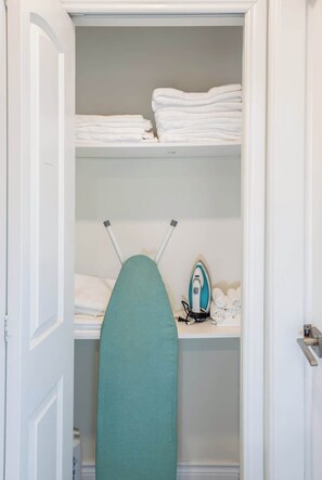 A closet with shelves holding folded towels, an ironing board, and an iron. - Central Van 3BR Upper Suite - Near Skytrain (Vancouver)