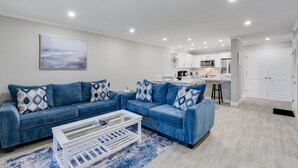 Een moderne woonkamer met een blauwe modulaire bank, een witte salontafel en een keuken op de achtergrond.