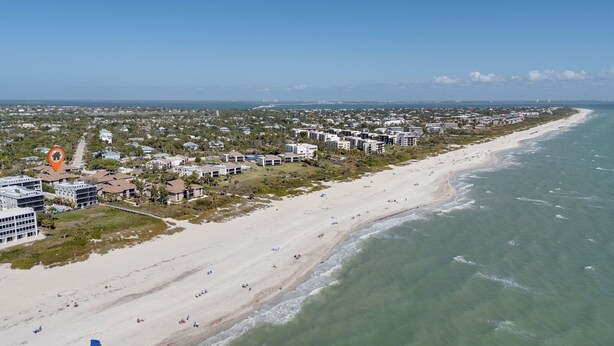 Luchtbeeld van een kustgebied met een strand, gebouwen en een heldere lucht.
