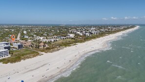 An aerial view of a coastal area with a beach, buildings, and a clear sky. - Coquina Beach 4B | Gorgeous Ground Level Beach Residence | Steps to the Sand (Sanibel)