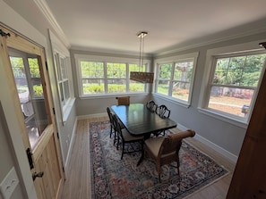 A dining area with a table and chairs, large windows, and a hanging light fixture.