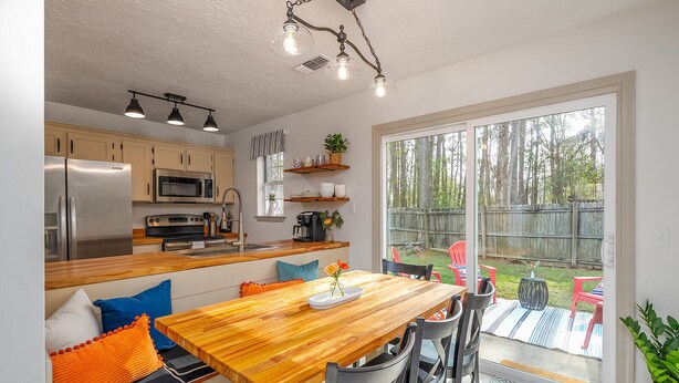 A modern kitchen with stainless steel appliances, a wooden dining table, and a view of a backyard with a wooden fence.