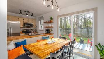 Une cuisine moderne dotée d’appareils électroménagers en acier inoxydable, d’une table à manger en bois et donnant sur un jardin avec une clôture en bois.