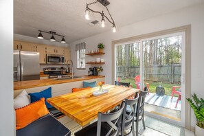 A modern kitchen with stainless steel appliances, a wooden dining table, and a view of a backyard with a wooden fence. - Southern Getaway near Downtown Savannah & Tybee (Richmond Hill)