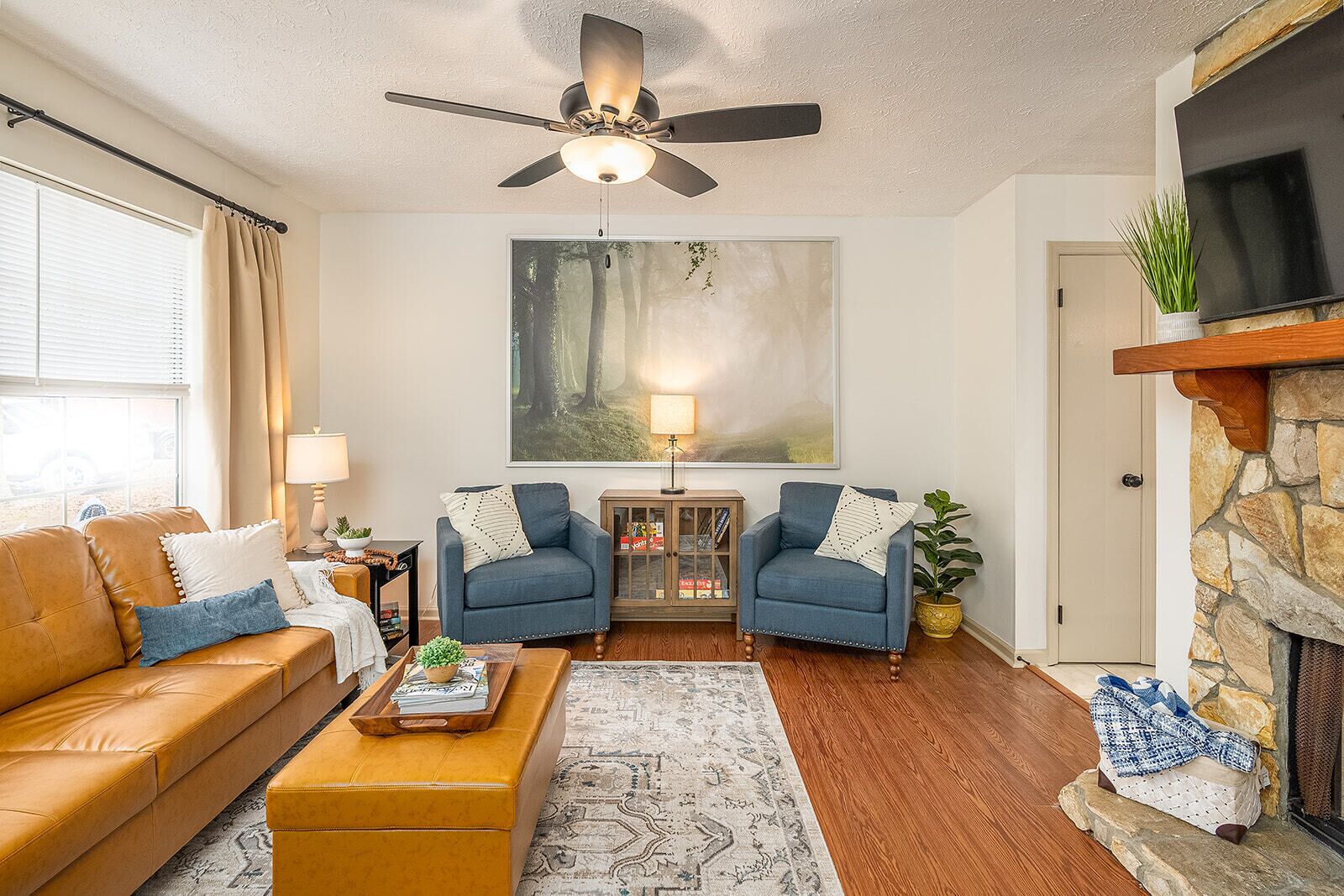 Un salon comprenant un canapé, deux fauteuils, une table basse, une cheminée, un téléviseur et un ventilateur de plafond.