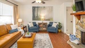 A living room with a sofa, two armchairs, a coffee table, a fireplace, a TV, and a ceiling fan.