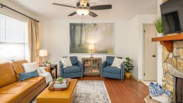 Un salon comprenant un canapé, deux fauteuils, une table basse, une cheminée, un téléviseur et un ventilateur de plafond.