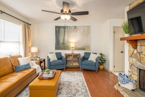 Un salon comprenant un canapé, deux fauteuils, une table basse, une cheminée, un téléviseur et un ventilateur de plafond.
