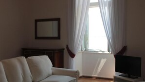 Una sala de estar con sofá, televisor sobre un mueble, chimenea y ventana con cortinas.
