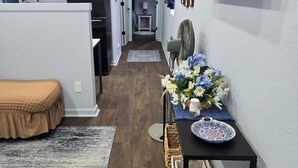 A narrow hallway with a bed on the left, a desk with a vase of flowers on the right, and a clock on the wall. - The Blue Goose, a charming house in Marshall, perfect for your getaway. (Marshall)