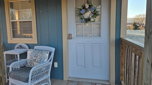 A porch with a white door, a wicker chair, and a welcome mat. - The Blue Goose, a charming house in Marshall, perfect for your getaway. (Marshall)