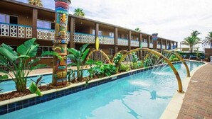 Un hotel con piscina, una fuente de estilo tiki y un edificio de varios pisos con balcones.