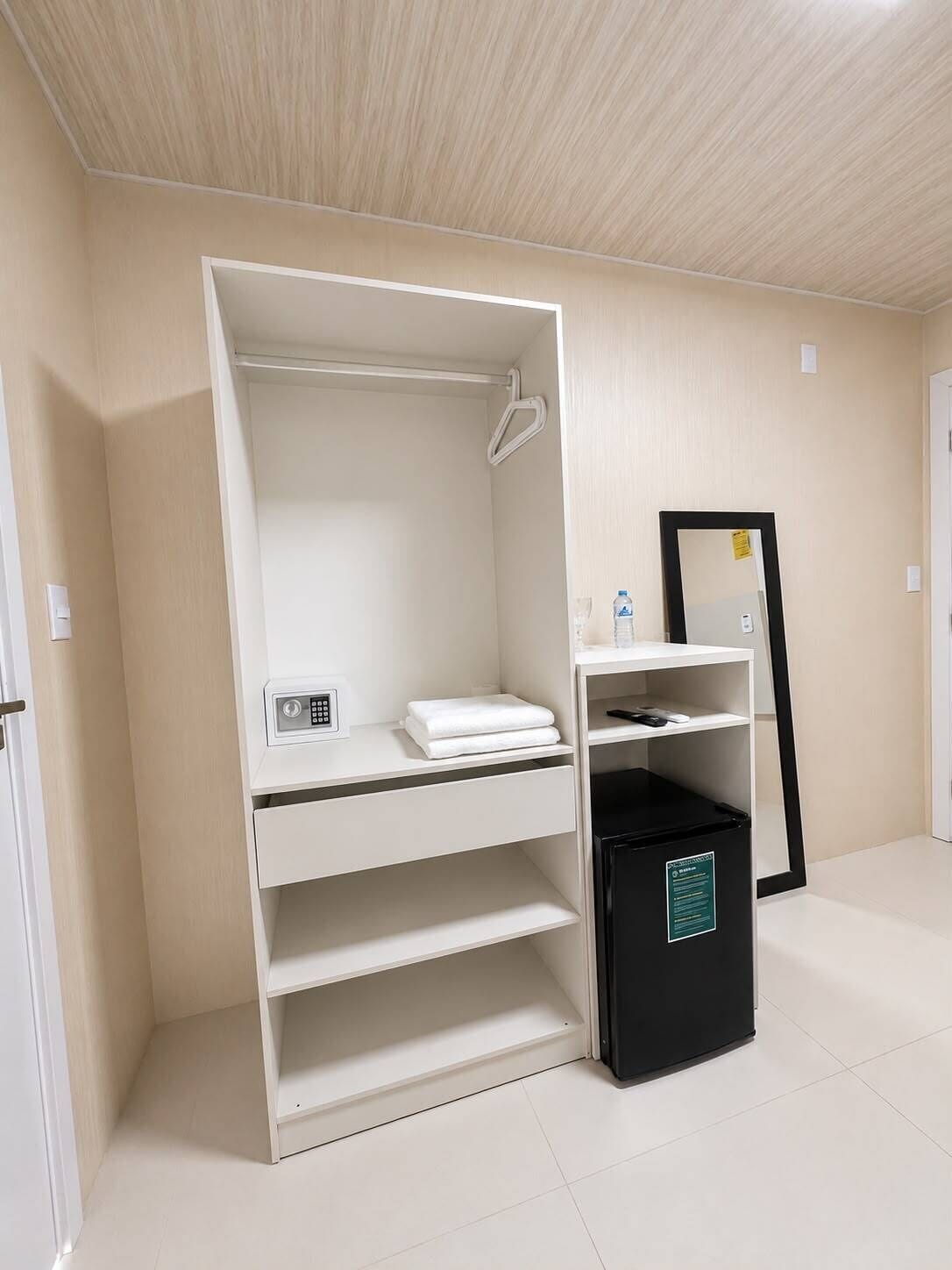 A room with a built-in wardrobe, a small desk with a computer, and a black trash bin.