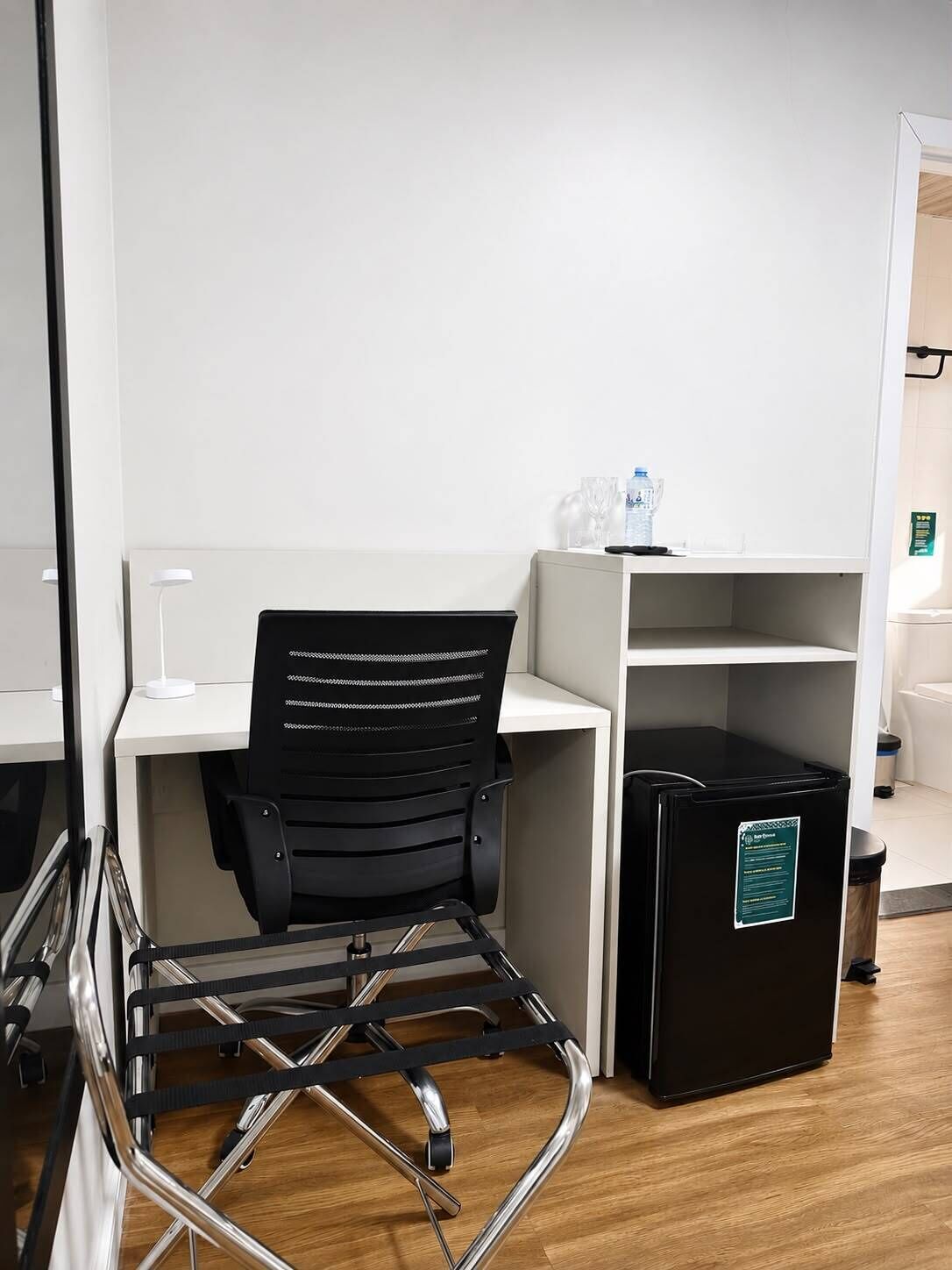 Un espacio de oficina moderno con una silla de escritorio negra, un escritorio blanco, un cubo de basura negro y una pared blanca.