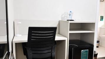 Un espacio de oficina moderno con una silla de escritorio negra, un escritorio blanco, un cubo de basura negro y una pared blanca.