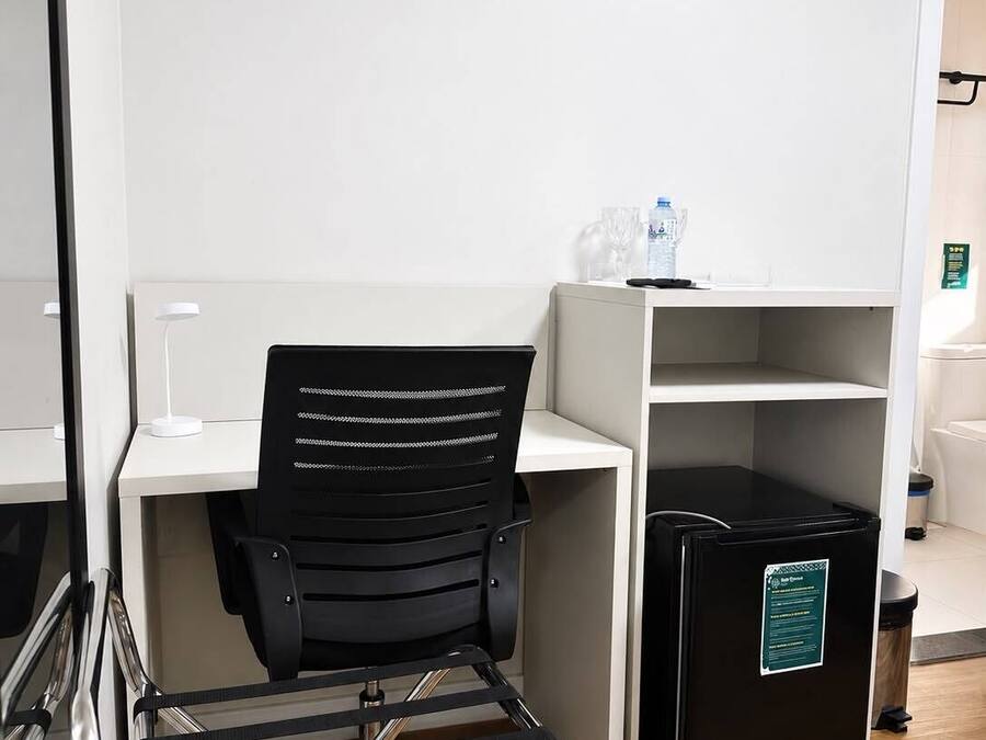 Un espacio de oficina moderno con una silla de escritorio negra, un escritorio blanco, un cubo de basura negro y una pared blanca.
