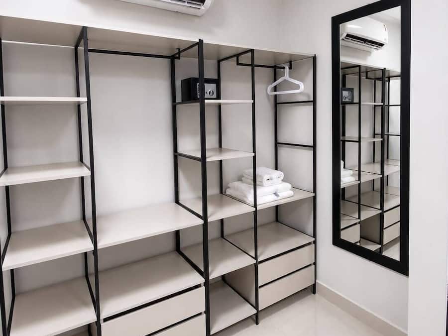 A modern closet with multiple shelves and hanging space, an air conditioning unit above, and a mirror on the wall.