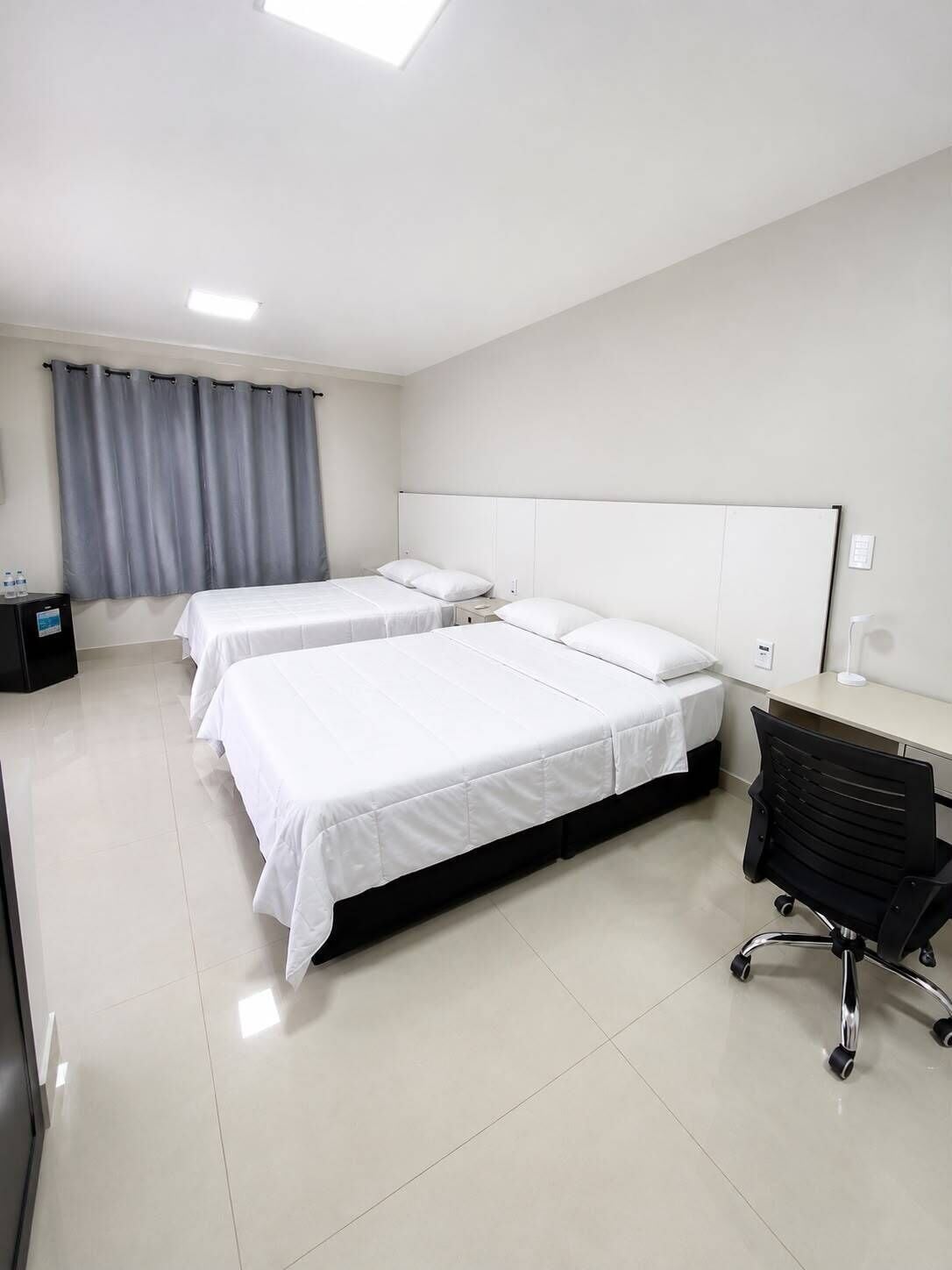 Quarto de hotel com três camas, uma escrivaninha e uma cadeira.